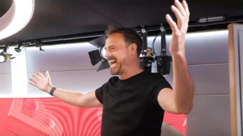 Jamie Theakston dressed in a black T-shirt and with arms outstretched arriving on the radio set of Friday's Heart Breakfast show