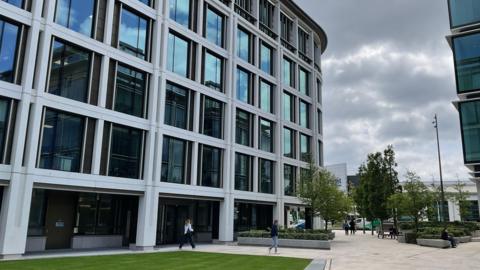 One of Jersey's finance buildings with greenery a walk way and some trees in front with people walking.
