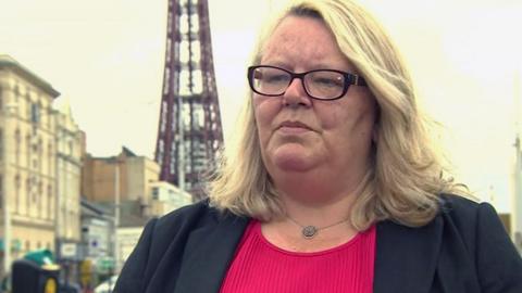 Lynn Williams, with blonde hair and wearing a red top and black jacket, stands in front of the rusty-red-framed Blackpool Tower