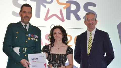 Deenah Elswaf (centre) proudly holds her award, flanked by EEAST Chief Operating Officer Darren Meads (left) and Chief Executive Neill Moloney (right), during the Stars of EEAST ceremony celebrating excellence in patient care.
