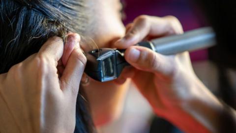 A woman has her ear inspected with an otoscope by an audiologist.