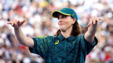 Raygun, wearing a t-shirt and cap, holds her arms out in front of her