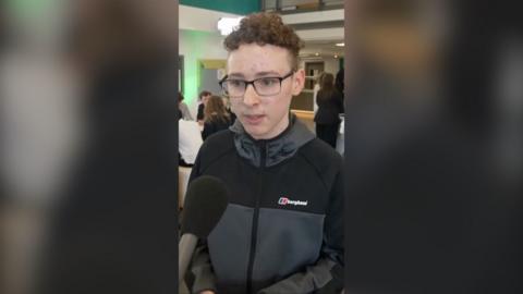 Young person in a zip up coat speaking into a microphone