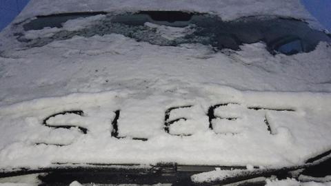 A snow-covered car with the word 'sleet' written in the snow on the bonnet