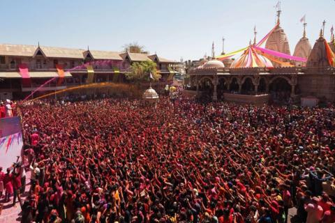 A crowd of people, some with their hands in the air, covered in colour for Holi festival