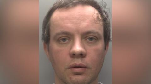 Police mugshot of Rick Parker - a man with wavy dark hair. He is clean shaven and is looking directly at the camera.