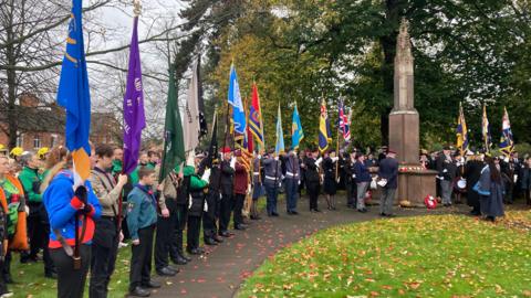 Image displays a series of flags arrayed around the war memorial in Bedworth, with a scattering of Armistice day poppies laying on the floor.