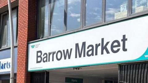 A building with glass windows and a large sign reading "Barrow Market".