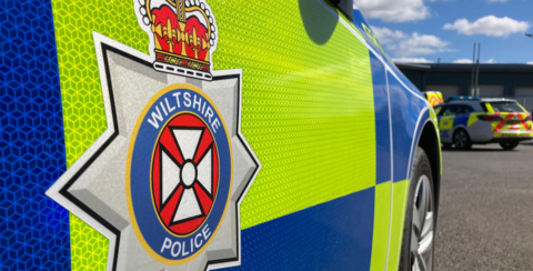 The side of a Wiltshire police car, featuring the Wiltshire Police logo and hi-vis rectangles of yellow and blue.