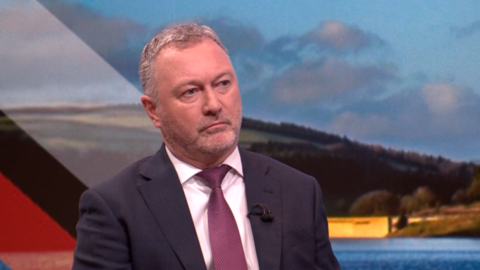 Steve Reed sitting down wearing a suit and tie