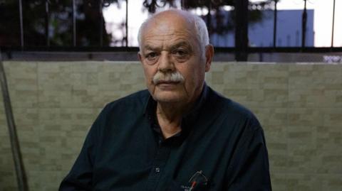 Kasem Abu al-Hija sits in a vigil for his family members. He is a man in his 60s with a grey moustache
