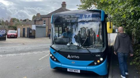 A bald man in a hoodie gets on a blue bus 