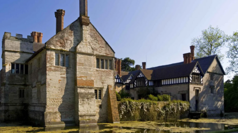 A large stone building with a black and white section to the side and water in front of it.