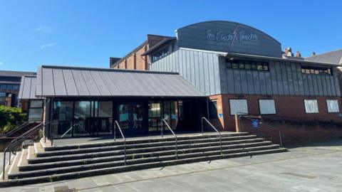 A large building made from bricks and grey panelling. It has a large sign reading The Electric Theatre and blank spaces that typically would advertise upcoming shows.