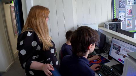 A teacher talking to two pupils who are working on computers in an IT lesson at Castlebridge School