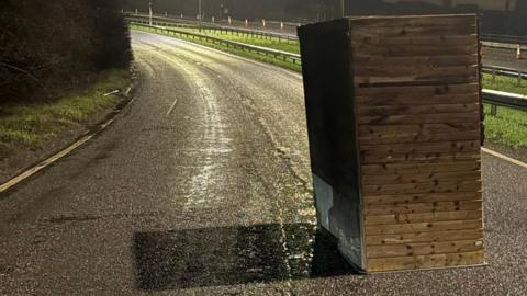 A wooden chicken coop in the middle of a dual carriageway.
