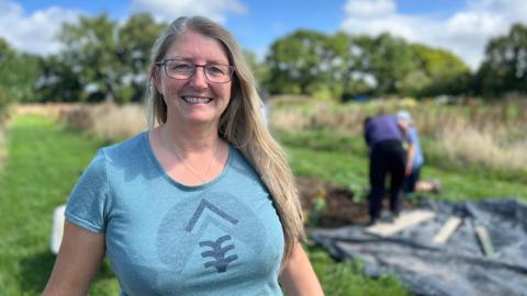 Sheena smiles at the camera as people dig in the field behind her