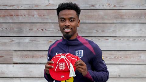 Angel Gomes holding his England cap