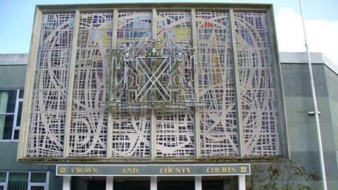 Outside of Plymouth Crown Court entrance with large mural with a lot of squiggly lines and the city's coat of arms.