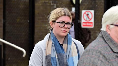 Ciara Corvan, with tied up blonde hair, wearing glasses, a blue and beige scarf and a grey jacket.