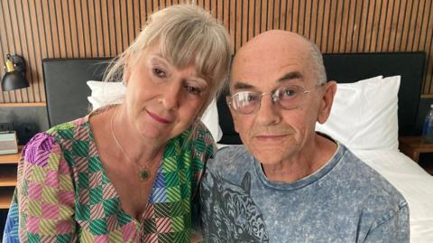 Karen McGory, wearing a multi-coloured top, is sitting next to Colin MCGrory, who is wearing a grey T-shirt with a tiger pattern on it. 