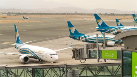 Planes with blue tails and marked "Oman Air" line up at Muscat International Airport.