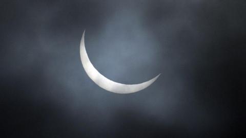 The sun obscuring the moon on a dark, cloudy night.