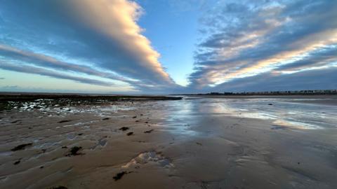 Striped clouds above a flat, wide beach