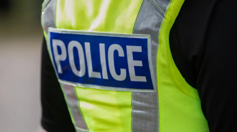 The back view of a British police officers vest. It is bright yellow and says the words POLICE in bold white lettering 