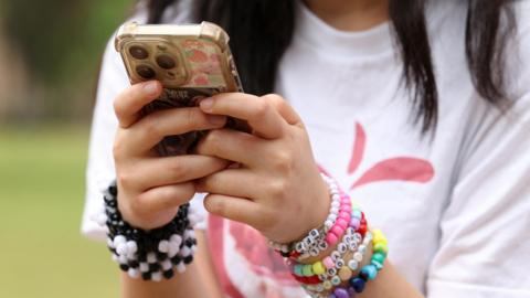 Teen girl wearing a clutter of colourful bracelets on her wrist as she types on her smartphone.
