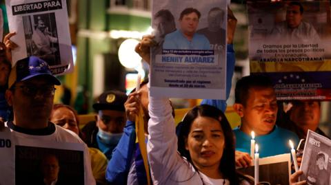 A group of protesters with a woman centred hold candles and signs of people who have been made political prisoners in Venezuela
