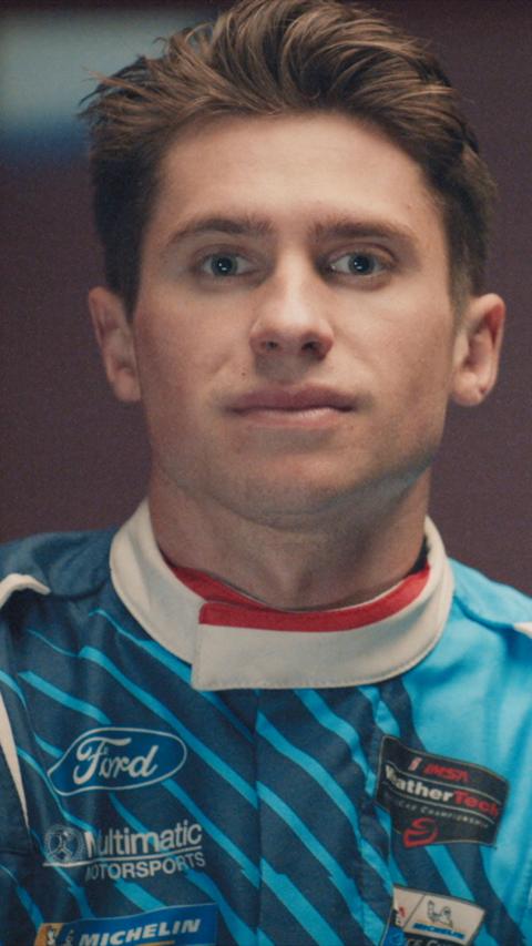 A man looking at the camera wearing a blue racing jacket