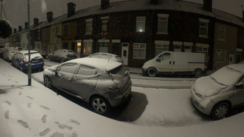 Snow on a street, with cars parked either side