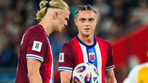Thelo Aasgaard (right) with short hair and a centre parting lines up alongside Erling Haaland with his distinct blonde ponytail in Norway's marroon, red, white and blue kit.