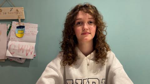 Anna Rose, na suidhe a' coimhead a' chamera agus coltas toilichte oirre.