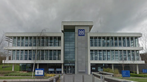 The headquarters of Durham Police is a three-storey white building mostly made of glass. It is surrounded by a small landscaped area. 