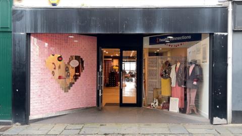 The shop front has a black frame round it and two big windows either side of the door.