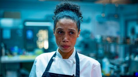 A worried and stressed looking chef, played by Vinette Robinson