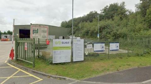 The waste and recycling centre at Launceston has five signs on iron railings with illegible small print headed by the word SUEZ. There is a single storey metal container in the yard which serves as an office.