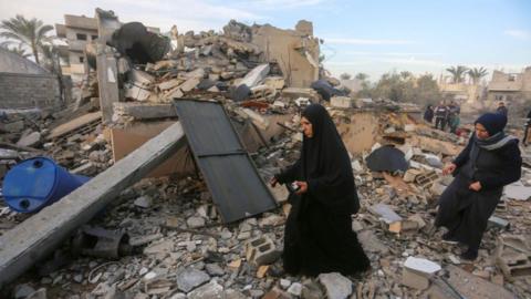 Two Palestinian women search and collect usable items among the rubble of a completely destroyed house in Gaza.