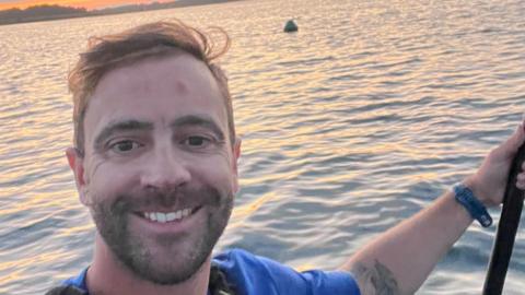 Smiling selfie of David Haze on his paddleboard with the sun setting in the background