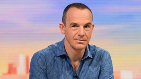 Martin Lewis wearing a dark blue shirt, sat in a TV studio.