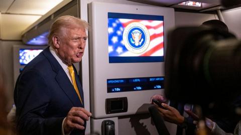 Trump in a blue suit and yellow tie talking to reporters