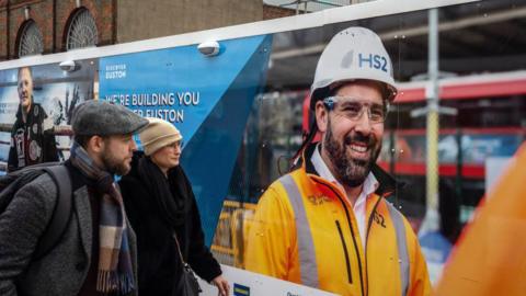 People walk alongside hoarding surrounding the HS2 site in Euston on 5 February, 2024 in London, England. 