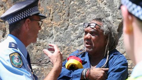 Wayne Wharton talks to a police officer while holding an Aboriginal flag