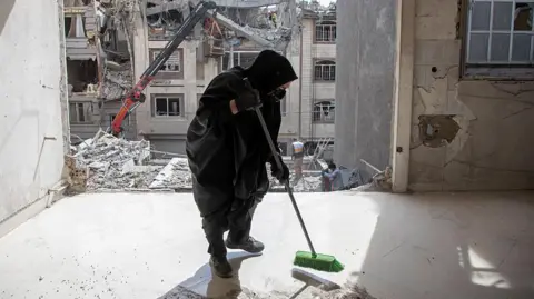  A resident cleans up debris in a damaged apartment across from another residential building following an airstrike in the early hours of March 27, 2026 in Tehran, Iran