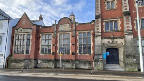 The old library building in Bideford which is set to be converted into a leisure centre. It has long windows across its main wall and a large black double door.