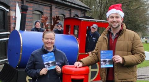 People from the Canal & River Trust stand near the stable block on the left. Two of the people are standing near the front by a postbox, with the man wearing a Santa hat.