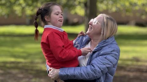 Vanellope is being held in the arms of her mum Naomi as they walk in the park