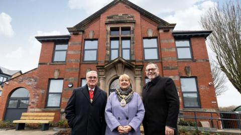 St Helens mayor Jeanette Banks stands between two men in front of a converted old dark brick building